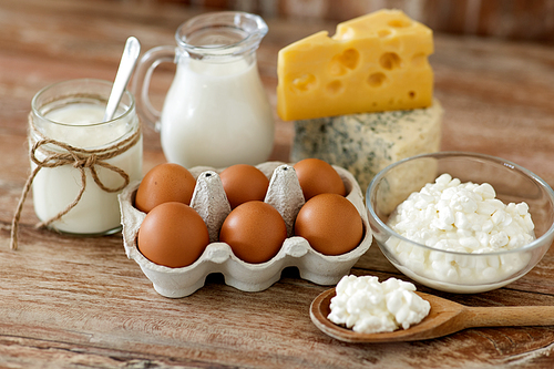 food and eating concept - close up of cottage cheese, jug of milk, homemade yogurt and chicken eggs on wooden table