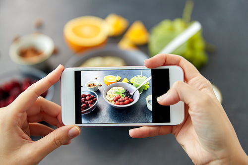 food, eating and breakfast concept - hand of woman taking picture of cereals in bowl with fruits, berries and juice with smartphone