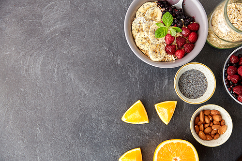 food and breakfast concept - oatmeal cereals in bowl with wild berries, fruits, almond nuts and poppy seeds on slate stone table