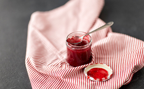 food, preserves and eating concept - mason jar with red raspberry jam with spoon on towel