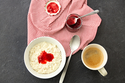 food and breakfast concept - porridge in bowl with jam, spoon and cup of coffee on slate stone table