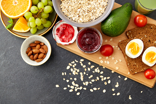 food, eating and breakfast concept - oatmeal cereals in bowl, fruits, almond nuts, jam and toast bread on slate stone table