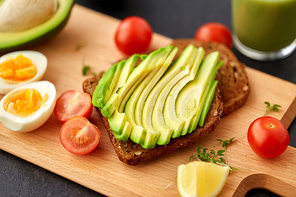 food, eating and breakfast concept - toast bread with sliced avocado, eggs and cherry tomatoes on wooden cutting board
