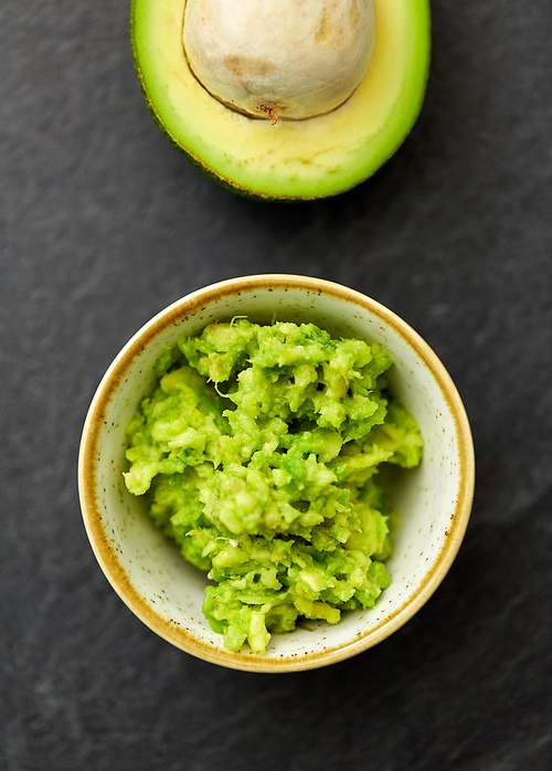 food, eating and vegetable concept - close up of mashed avocado in ceramic bowl on slate stone background