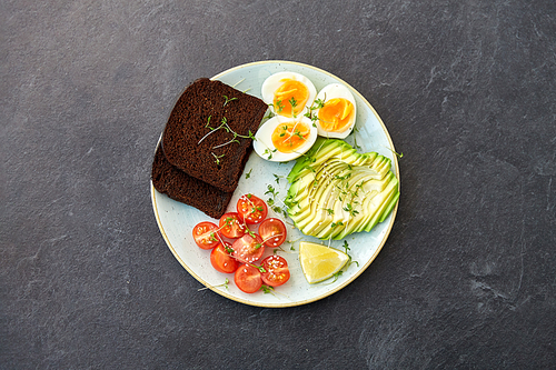 food, eating and breakfast concept - toast bread with cherry tomatoes, avocado, eggs and greens on ceramic plate