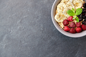food and breakfast concept - oatmeal cereals in bowl with wild berries, banana and peppermint on slate stone table