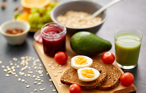 food, eating and breakfast concept - toast bread with eggs, cherry tomatoes, avocado and glass of juice on wooden cutting board