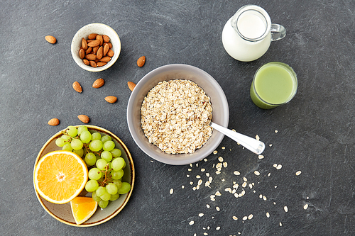 food and breakfast concept - oatmeal cereals in bowl, fruits, almond nuts, glass of juice and jug with milk on slate stone table