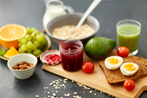 food, eating and breakfast concept - jar with raspberry jam, toast bread, eggs and cherry tomatoes on wooden cutting board