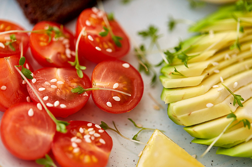 food, eating and breakfast concept - close up of cherry tomatoes and sliced avocado with thyme and sesame on ceramic plate