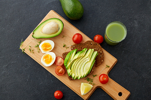 food, eating and breakfast concept - toast bread with sliced avocado, eggs, cherry tomatoes and greens on wooden cutting board