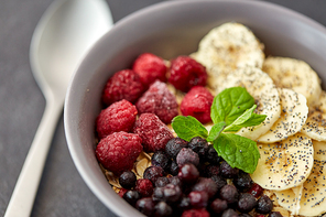 food and breakfast concept - close up of cereals in bowl with wild berries, banana and peppermint on slate stone table