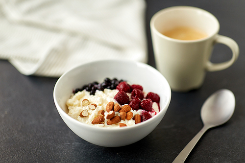 food and breakfast concept - porridge in bowl with wild berries, almond nuts, spoon and cup of coffee on slate stone table