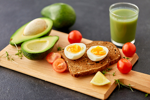 food, eating and breakfast concept - toast bread with eggs, cherry tomatoes, avocado and greens on wooden cutting board