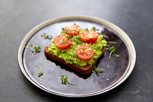 food, eating and breakfast concept - toast bread with mashed avocado, cherry tomatoes and greens on ceramic plate