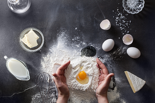 Woman's hands knead dough on table with flour, eggs and ingridients. Top view.
