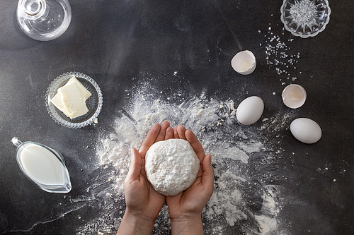 Woman's hands knead dough on table with flour and ingridients. Top view.