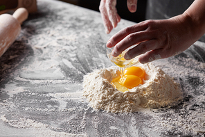 On a kitchen table a pile of flour with yolks, baker pours the squirrels into the flour. Step-by-step preparation of the dough