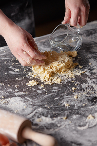 A woman in a black apron kneads the dough by adding water to the kitchen table. Preparation of dough for baking