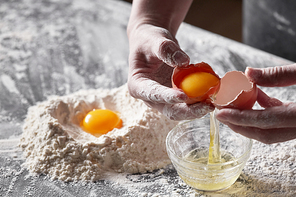 A women's hands baker shares an egg on the background of a kitchen table with flour. The concept of a step-by-step preparation of a dough for baking