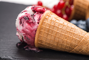 Ice cream cone with scoop of red fruits on dark textured background.