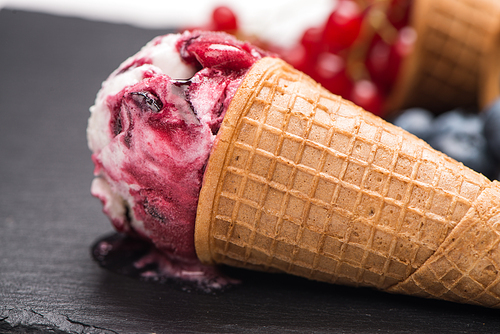 Ice cream cone with scoop of red fruits on dark textured background.