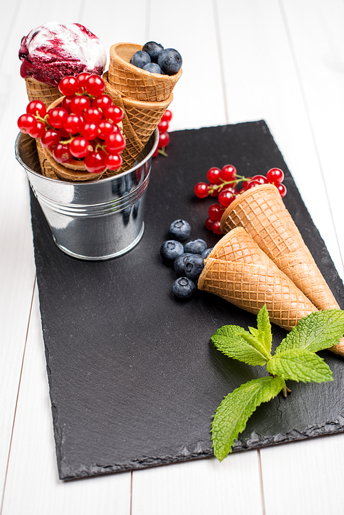 Red fruits ice cream cone on black slate board.