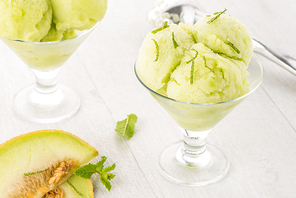 Close up of melon flavored ice-cream with mint and melon on a white table.