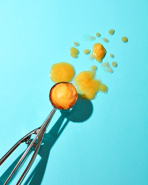 Creative composition from a ball of yellow ice cream on a metal spoon on a blue glass background with shadows. Food modern style.