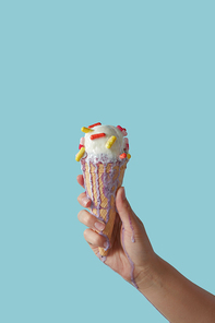 A female hand holds a melting fruit ice cream with colored pills on a blue background with copy space. Cold summer dessert, the concept of a sore throat