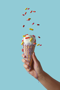 A female hand holds white delicious dessert in a waffle cone on a blue background with copy space. The concept of summer catarrhal diseases and their treatment.