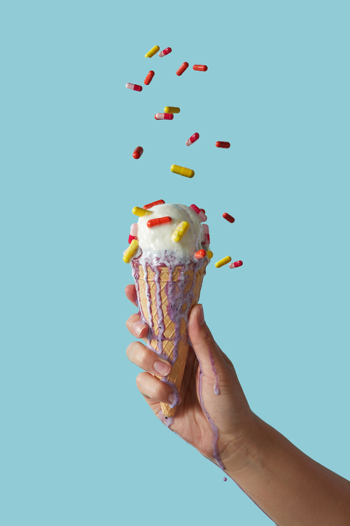 A female hand holds white delicious dessert in a waffle cone on a blue background with copy space. The concept of summer catarrhal diseases and their treatment.