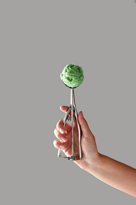 A metal scoop with pistachio ice cream. Girl's hand holds on a gray background a copy space for text.