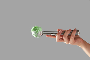 A female hand holds a metal scoop with green fruit ice cream on a gray background with space for text. Cold summer dessert.