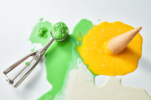 Multicolored splashes of melted ice cream. Scoop of green ice cream and a fallen waffle cone with a yellow ice cream on a blunder background with a copy of the space.Top view
