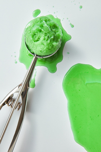 A metal scoop with a green mint ice cream on a gray background with drops and splashes. Summer dessert concept. Top view