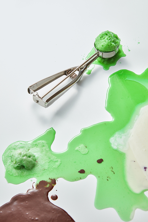 A pattern of white, green, brown drops and ice cream flashes with a metal scoop of apetized ice cream on a gray background. Space for your text. Top view