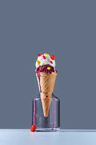 A delicious dessert in a waffle cone with red and yellow pills and lollipops stands in a glass jar on gray background. The concept of summer catarrhal diseases and their treatment with place for text.