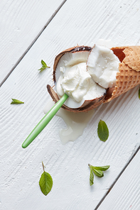 Vanilla ice cream in a waffle cone with a spoon and coconut on a white background with mint leaves On white wooden background