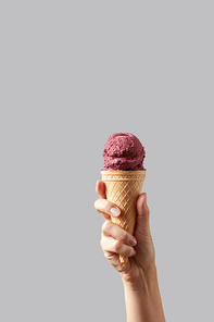 Berry red ice cream in the form of ball in a waffle cone in a famale hand on a gray background. Summer concept with space for text.