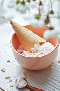 Delicious ice cream with waffle cone in a plate and flowers in white wooden background