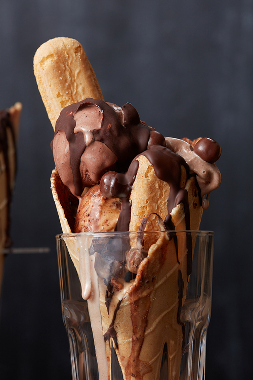 Chocolate ice cream waffle cone with biscuits, chocolate candies and syrup in a glass