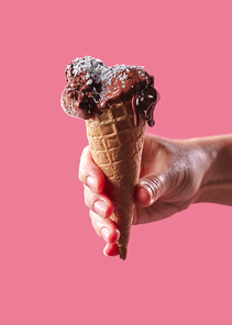 Ice cream with coconut flakes in a waffle cone holds the hand of a man on a pink background with a space for text. Cool summer dessert.