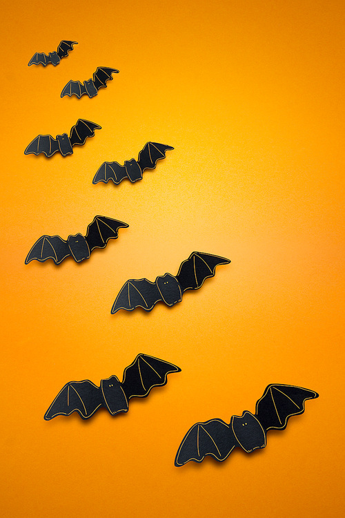 Creative halloween concept photo of bats made of paper on orange background.