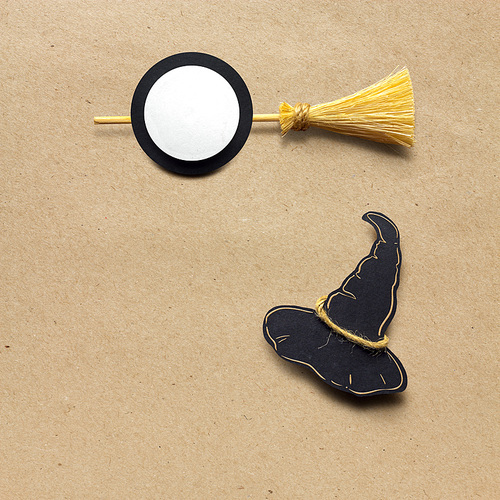 Creative halloween concept photo of witches hat and broom made of paper on brown background.