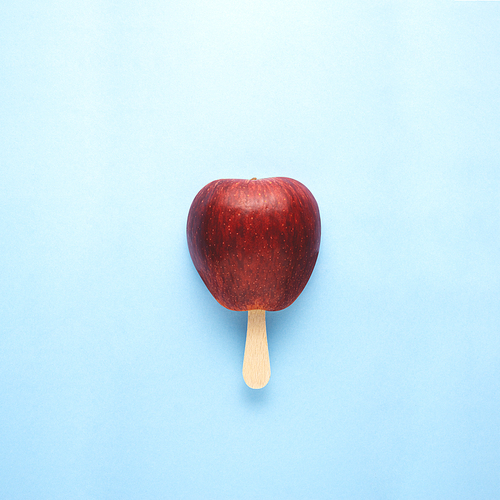 Creative concept still life food diet health photo of apple fruit on stick in shape of ice cream popsicle on blue background.