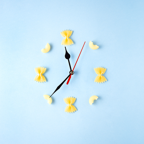 Creative concept still life food diet health photo of raw pasta spaghetti in shape of clock with hands on blue background.