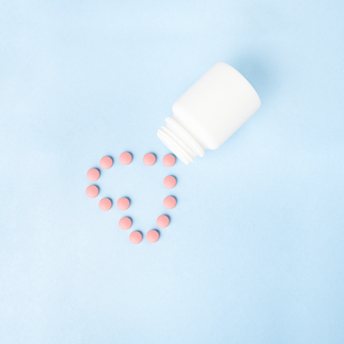 Creative concept still life health medicine photo of pills drugs cure in shape of heart with bottle on blue background.