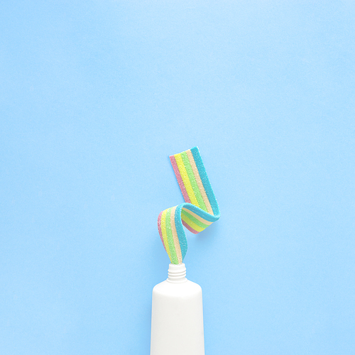 Creative concept still life food health photo of toothpaste tube with jelly marmalade candy marshmallow on blue background.