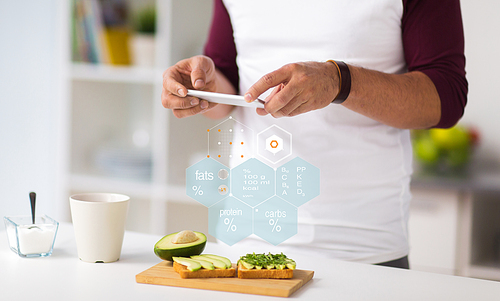 healthy eating, people and technology concept - close up of man with smartphone having vegetable sandwiches for breakfast at home kitchen over nutritional value chart
